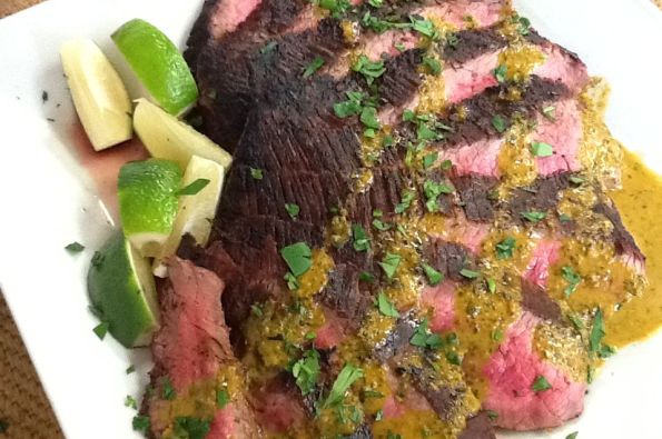 Grilled Chimichurri Flank Steak, with more drizzled on top and some lime wedges on the side.